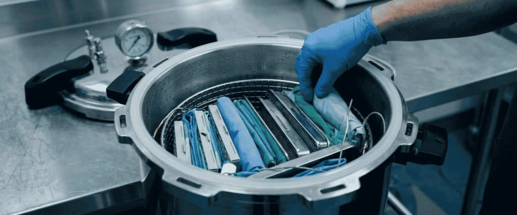 BKM-P18I Portable Autoclave with gloved hand placing wrapped medical instruments inside for sterilization