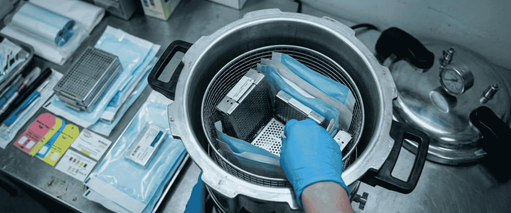 BKM-P18I Portable Autoclave with surgical instruments and blue sterilization pouches, handled by a gloved technician