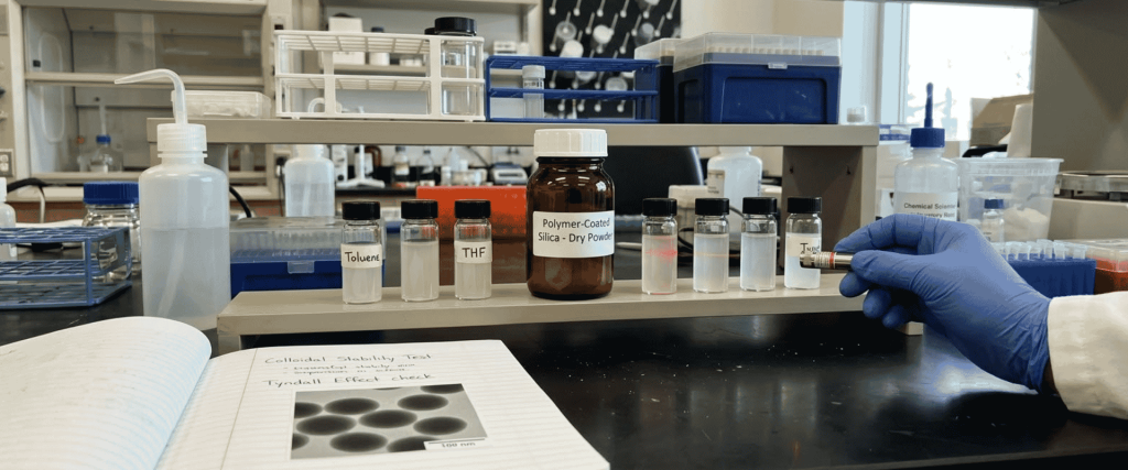Ultrasonic Polymer-Coated silica drying powder and laboratory samples on a bench, with a gloved researcher handling a vial