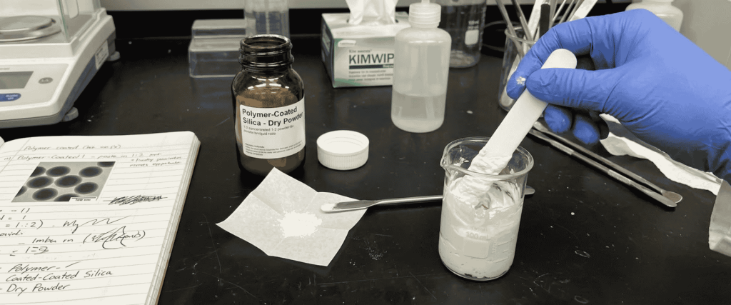 Ultrasonic Polymer-Coated silica powder mixed in a laboratory beaker with a spatula and gloved hand