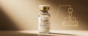 Bottle of clear medicine vial labeled "1um" with gold cap, soft studio lighting and schematic lab equipment drawing to right. 