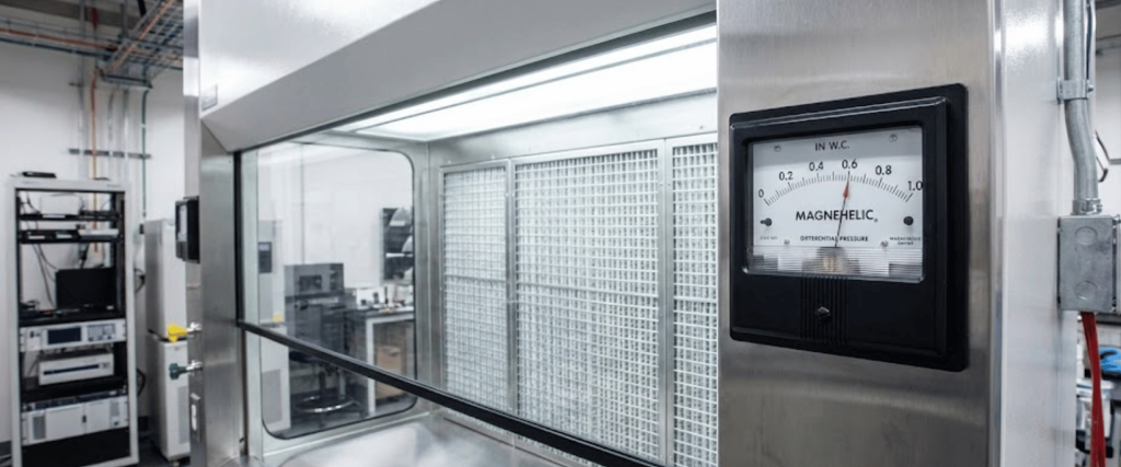 Laboratory clean hood with Magnehelic pressure gauge, filtration panels and technician working at a bench in the background