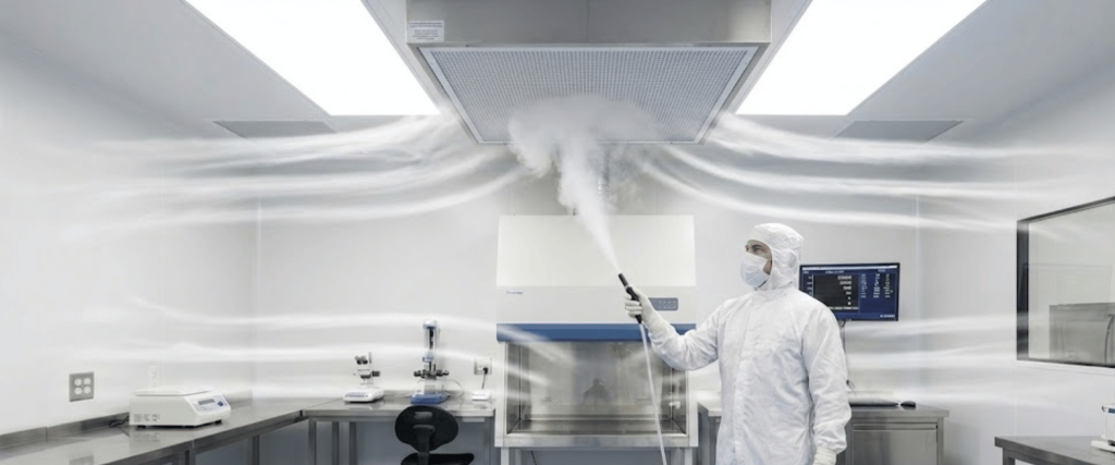 Laboratory technician in full cleanroom suit disinfecting hood with fogger under ceiling air vents, white sterile lab environment, instruments