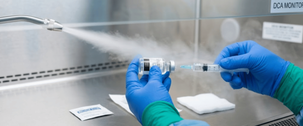 Medical technician in gloves drawing vaccine into a syringe inside a sterile hood, labeled [USP 797], ready for compounding and administration