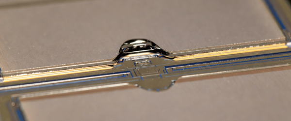Particle close-up on a microchip surface with reflective liquid droplet and intricate circuitry details