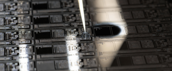 Particle inspection on a microchip wafer with a probe under bright lab light, showing detailed semiconductor patterns