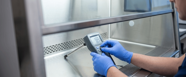 USP 800 gloved technician measuring airflow inside a biological safety cabinet with digital gauge for sterile compounding compliance 