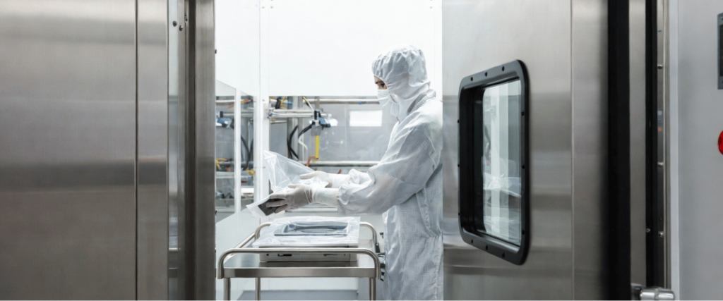 ISO Class 5 Cleanroom technician in protective suit handling sterile equipment inside a stainless steel controlled environment