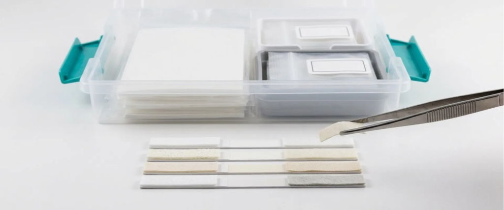 Lateral Flow test strips and tweezers beside a sample storage box on a white laboratory surface