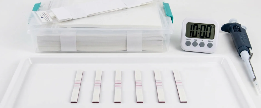 Lateral Flow test strips arranged on a white tray with timer and tool, showing multiple sample results in a clinical setup