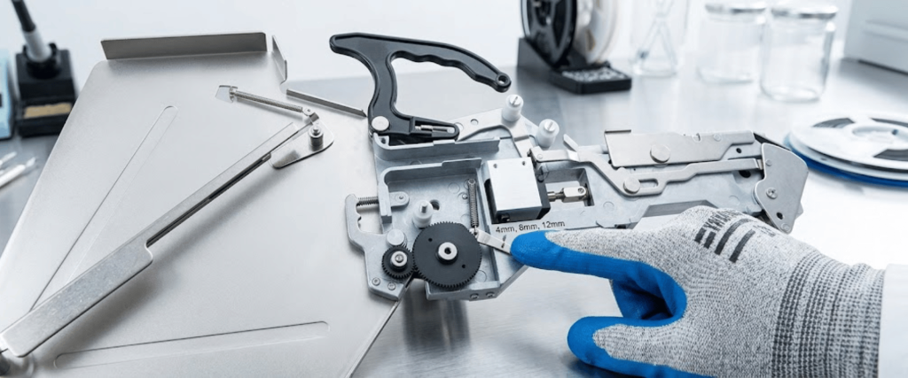 Yamaha CL 12mm component assembly close-up with precision metal parts and a gloved hand pointing to a machine